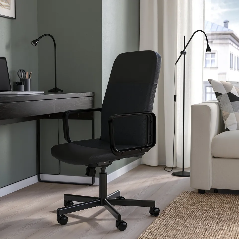 Modern office setup featuring black RENBERGET chair, sleek desk, and cushioned sofa, all bathed in natural light from a large window.
