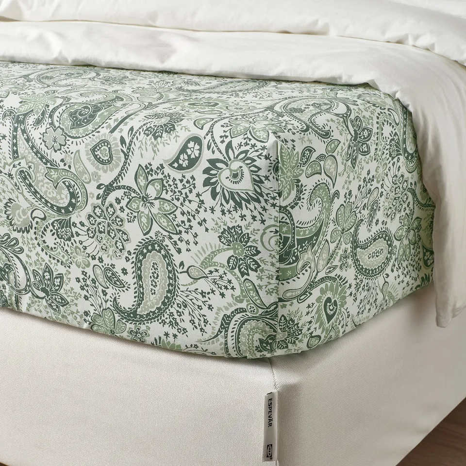A bed with a fitted sheet featuring a green and white paisley pattern, elastic edges, and soft cotton/viscose blend.