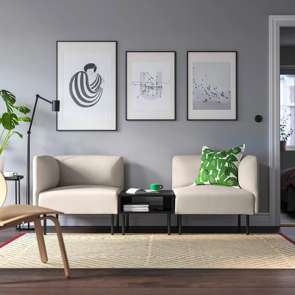 Modern living room with 2 beige sofas, art, 2 side tables, lamp, plant, large patterned rug.