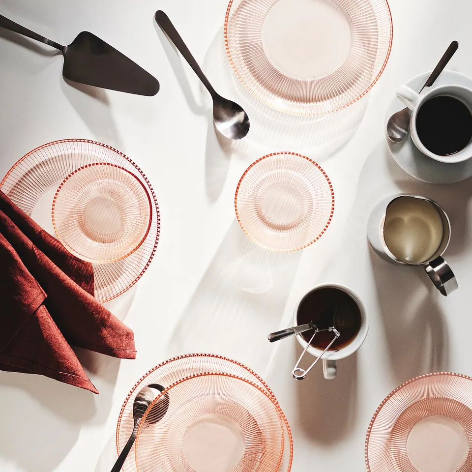 Top view of pink HAVSGÄDDA plates, glass. Surrounded by spoons, cups, knife, napkin. Smaller than cups, bigger than spoons.