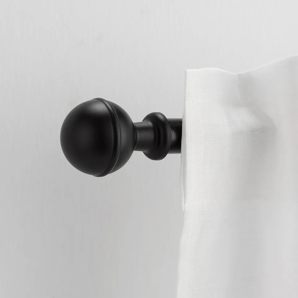 Depicts a black spherical ALVARSTÅNDS finial on a white curtain rod. Its small and elegant, suitable for home decor.