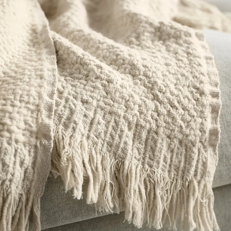 Beige handwoven throw blanket with fringes, showcasing a textured, natural-looking pattern.