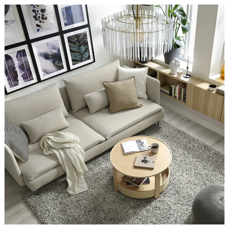 Modern living room: beige SÖDERHAMN sofa, cushions, round coffee table, patterned rug, chandelier, framed art, sideboard, and plants.