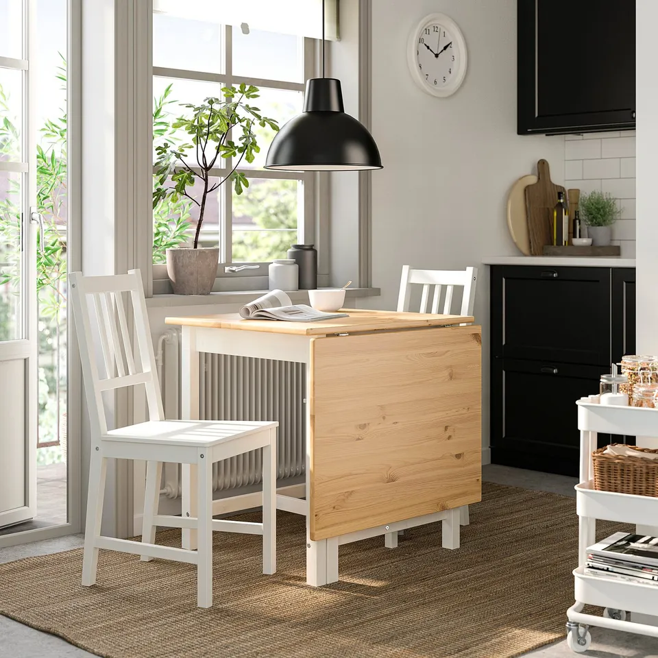 Modern kitchen with white drop-leaf table and chairs, wooden top by large window, black pendant lamp