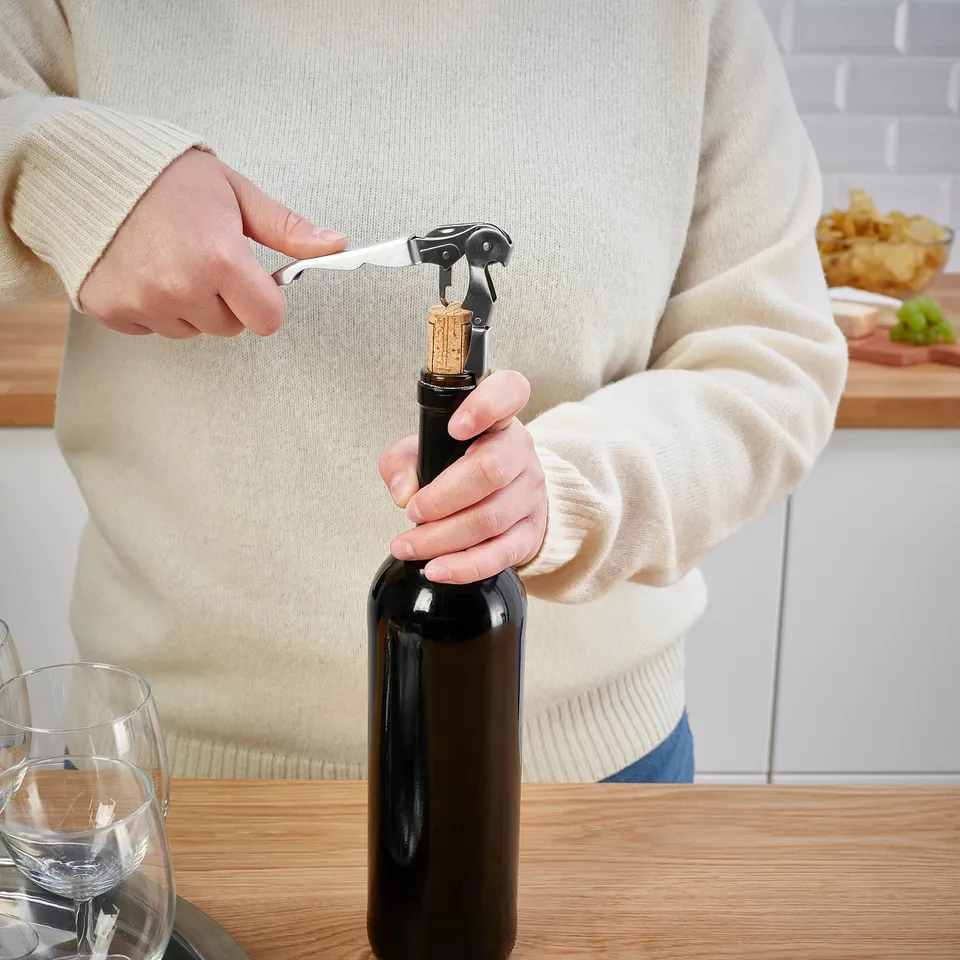 Person opening wine bottle with corkscrew, effortlessly pulling cork.