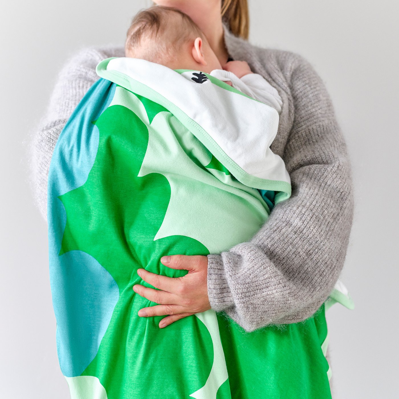A person holding a baby wrapped in a green and white blanket with leaf patterns, ideal for napping and comfort.