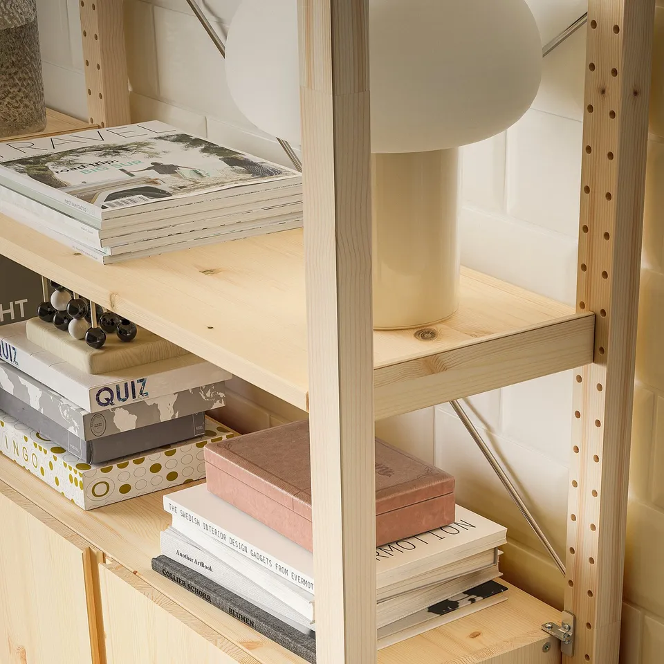 Wooden shelving unit with adjustable shelves holding books and boxes. Lamp sits on top.