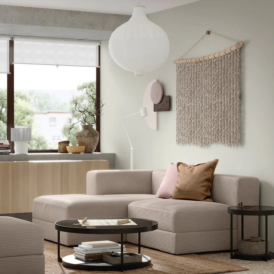 Cosy living room with JÄTTEBO modular sofa in light beige, featuring pillows, a coffee table with books, and large window with a view.