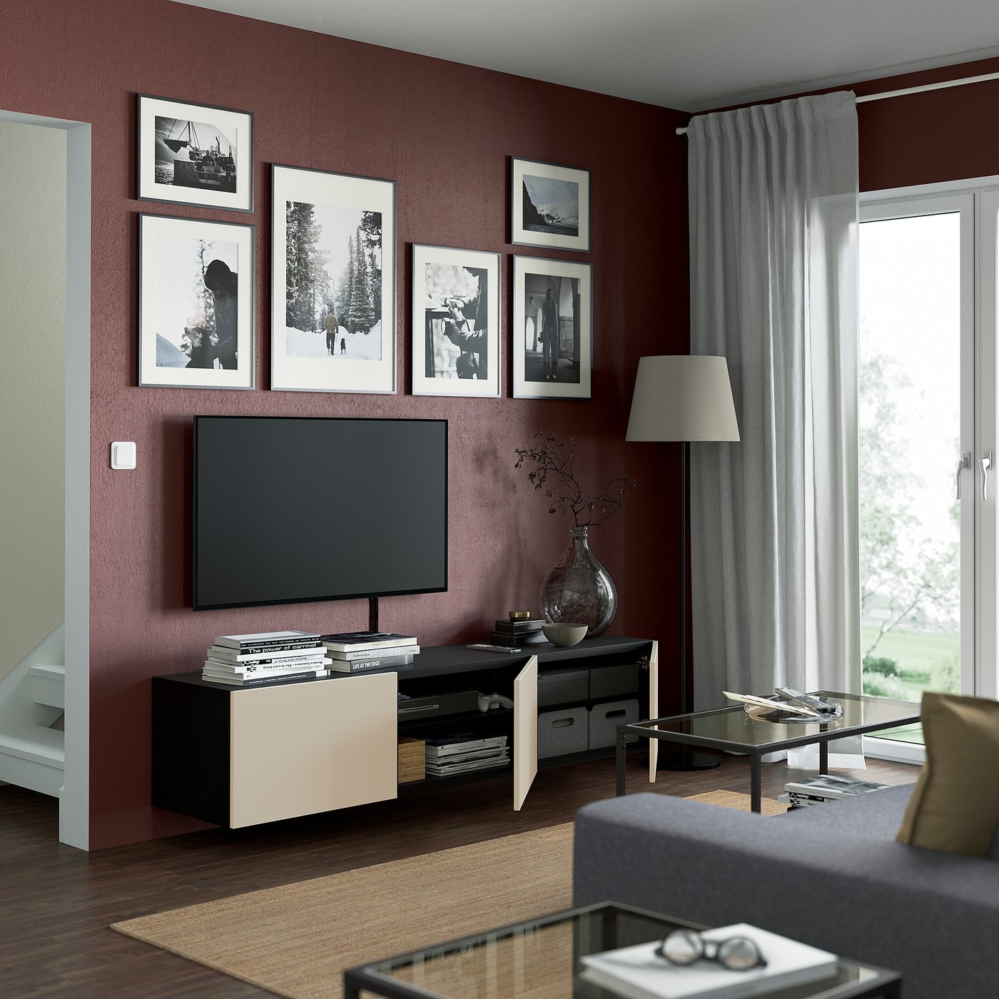 Modern living room with maroon walls, BESTÅ tv bench, flat-screen tv, books, vase, gallery wall, floor lamp, glass coffee table with magazines.