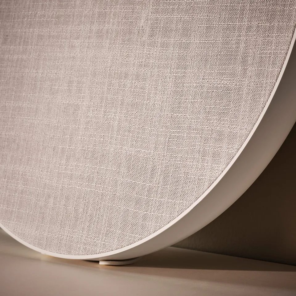 Close-up of SOLSKYDD speaker, white, curved design, fabric cover.