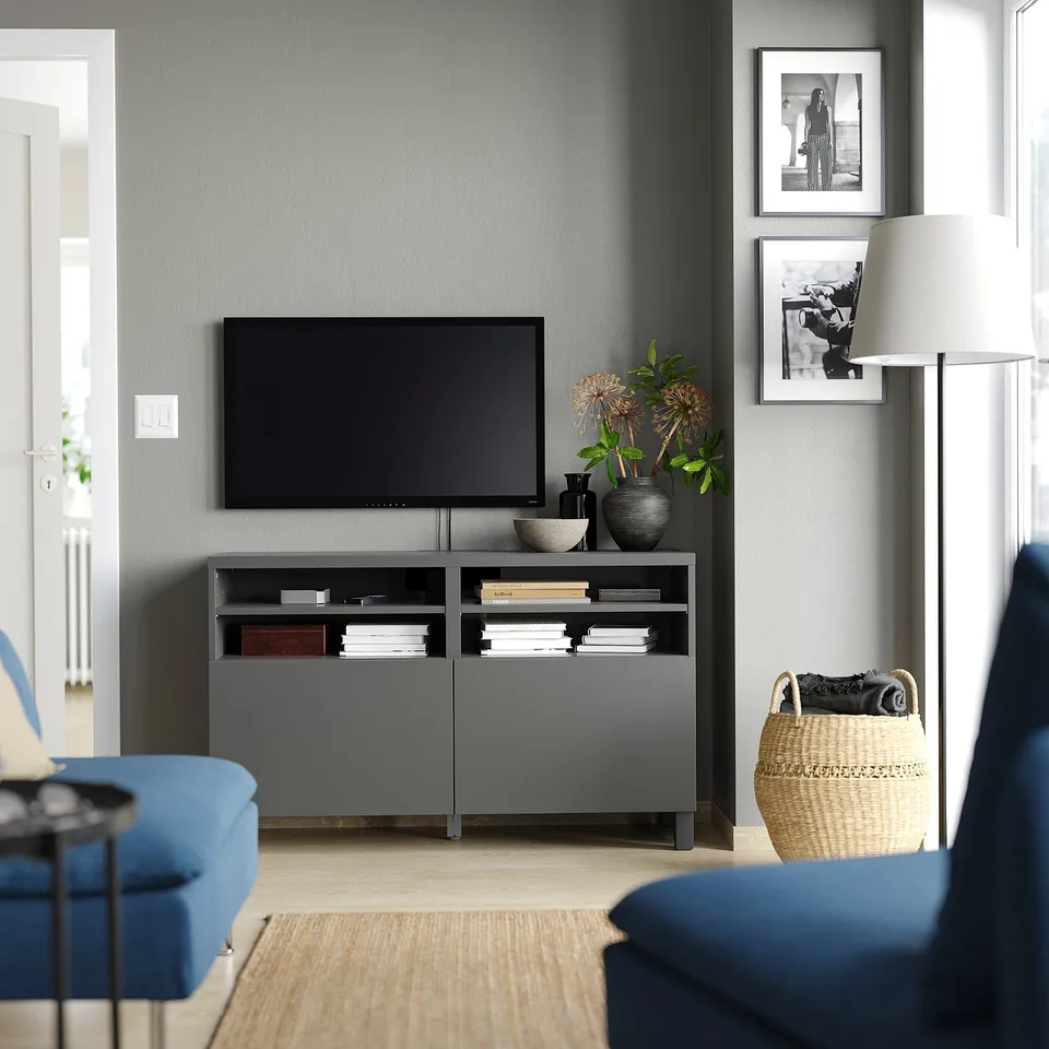 Modern living room with grey BESTÅ tv bench, blue sofa, lamp, pictures. Tv on stand, books, vase, wicker basket.