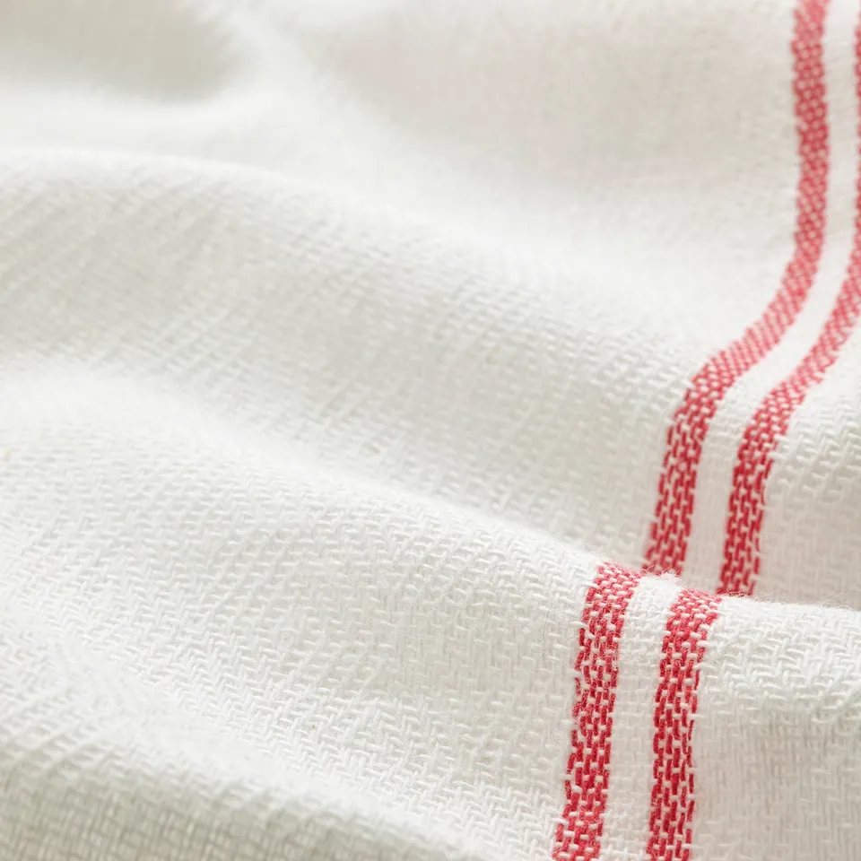 Close-up of stack of folded white towels with red hems, showing fabric texture and quality.