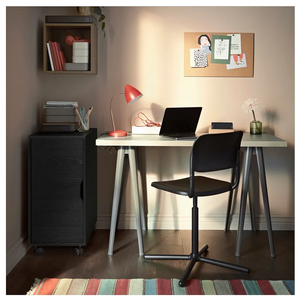 Modern home office setup with black and white desk, black chair, red lamp, wooden cabinet, and colourful rug.