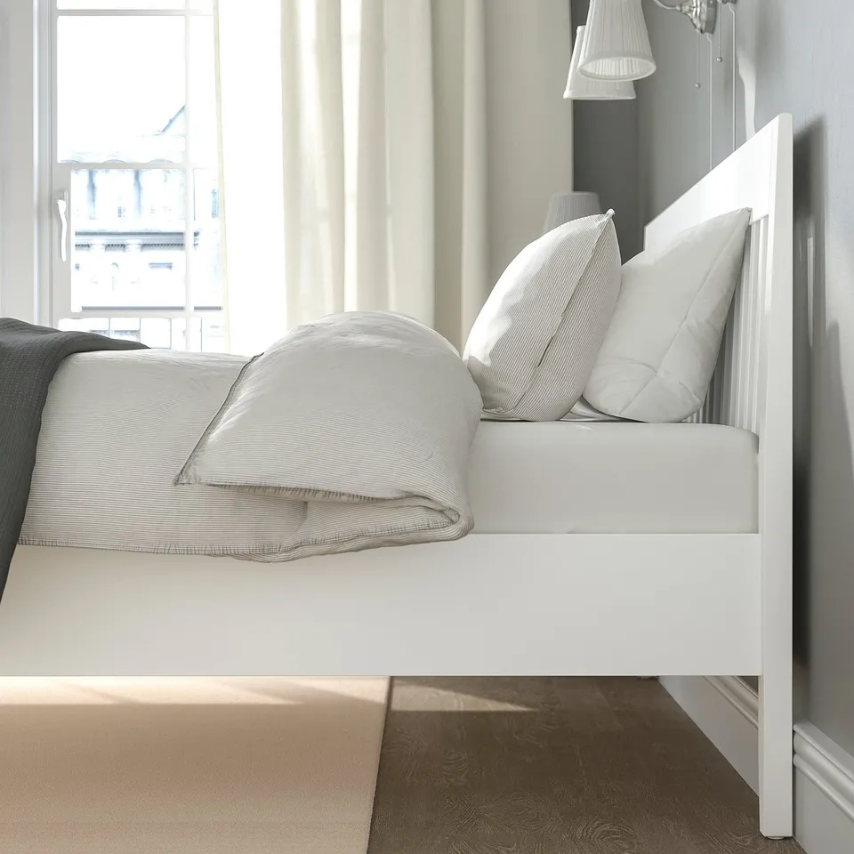 Neat bed with white linens, pillows, and headboard; sunlit view from window.