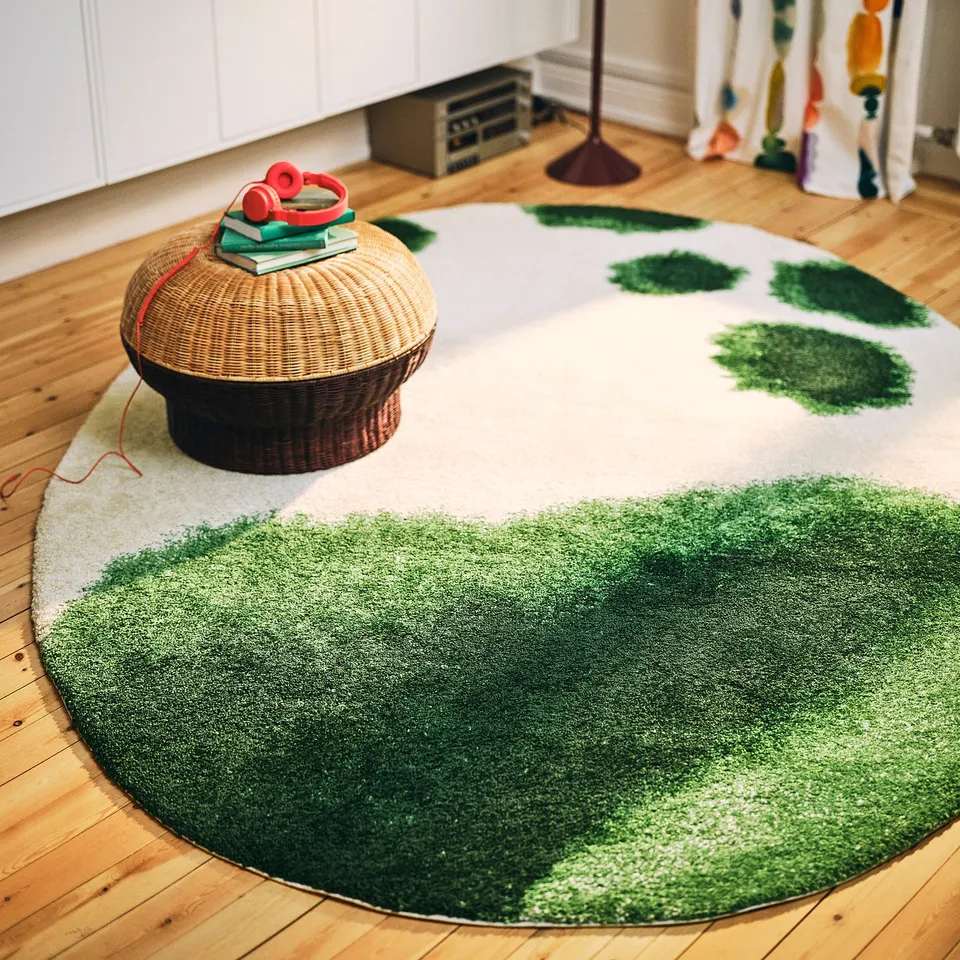 Circular IKEA footstool with woven rattan, small books, and red item on unique rug, near white furniture.