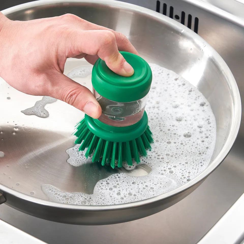 Person using a green VIDEVECKMAL brush with soap dispenser to clean a sink.
