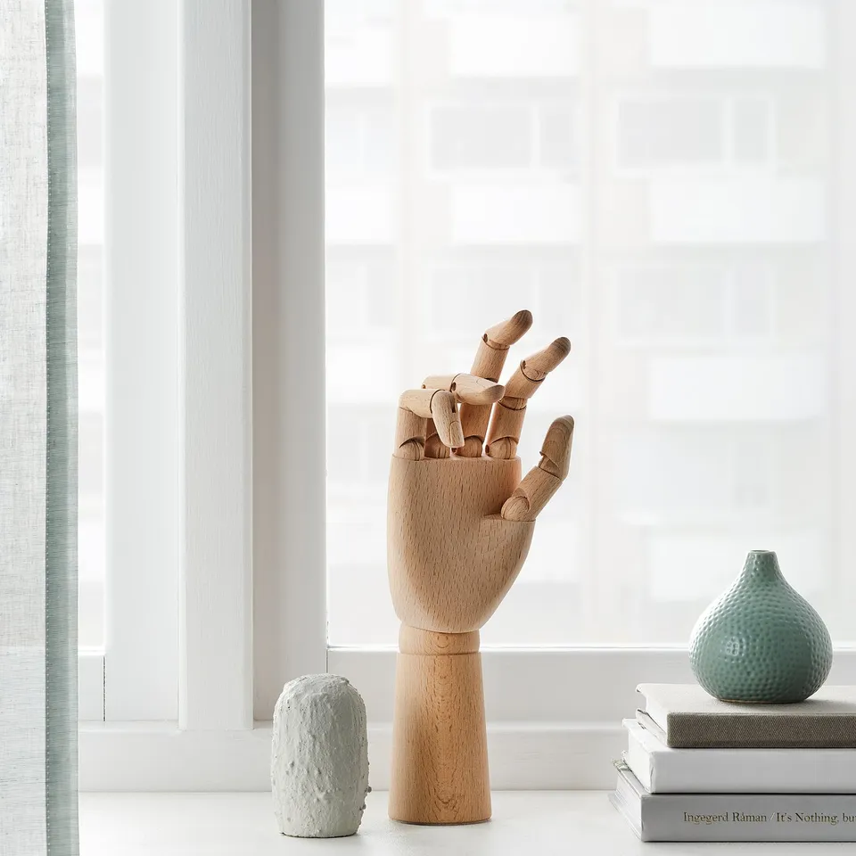 Wooden hand model on window sill, surrounded by two vases and books.