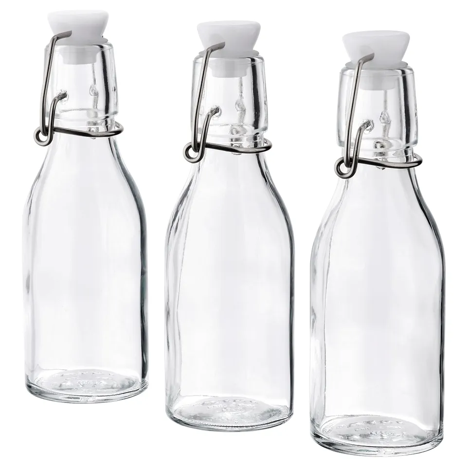 Three clear glass bottles with white stoppers and metal clips, arranged in a row. Ideal for storing liquids or condiments.