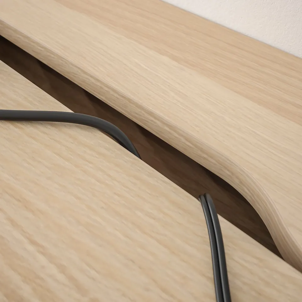 A close-up shows a wooden desk with built-in cable management. Cables run through narrow slots, keeping them tidy and organised beneath the tabletop.
