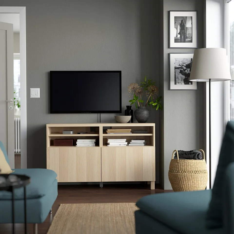 Modern living room with BESTÅ tv bench, tv, books, lamp, chairs, and blankets.
