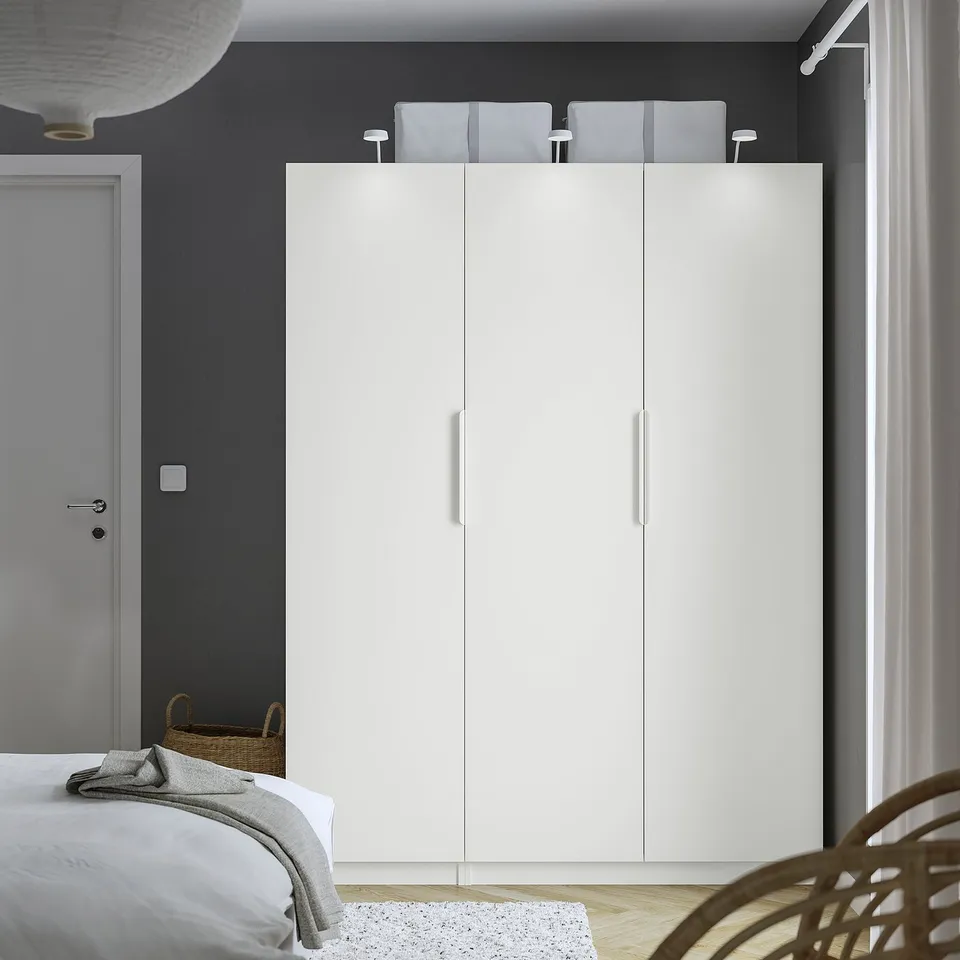 White PAX wardrobe fits well, tall and rectangular with three storage sections, contrasts dark wall, adds minimalist design.