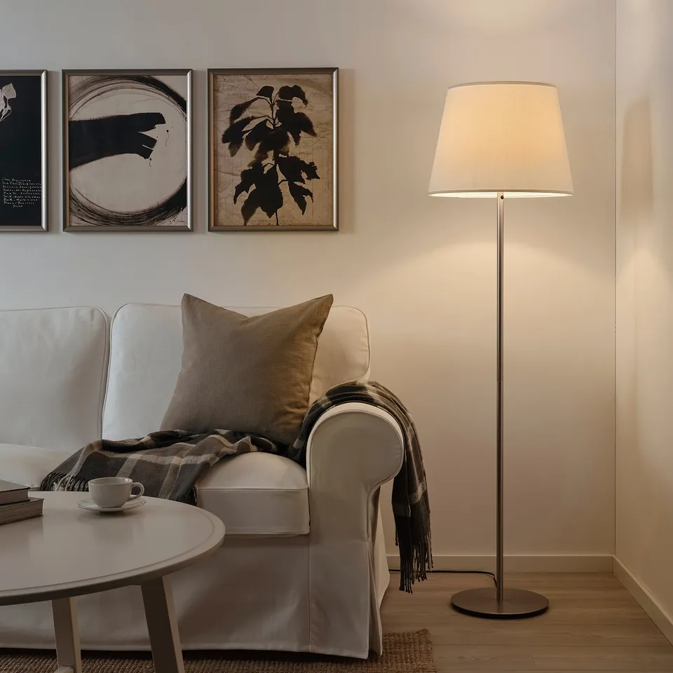 Cosy living room with a SKAFTET floor lamp, cream shade & base, next to a white couch, coffee table & art; warm, inviting space.