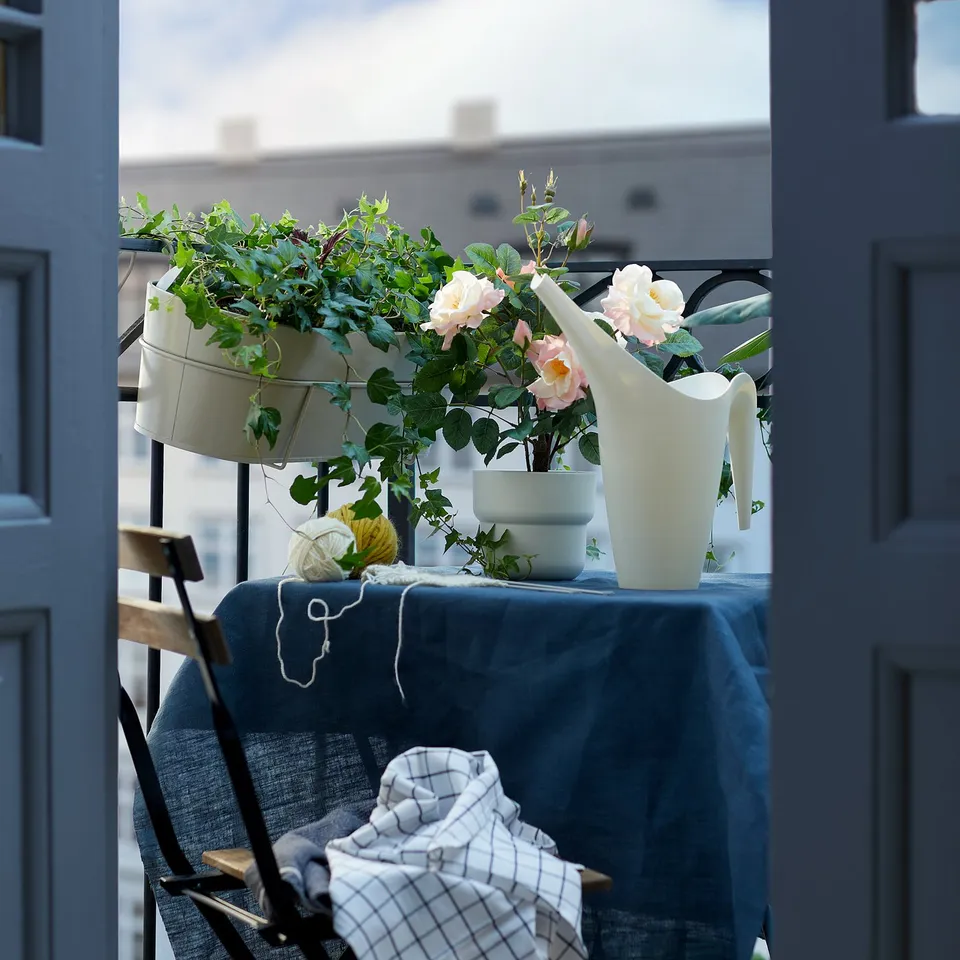 Balcony scene with white flowers, green plants in pots, blue tablecloth, and black foldable chair.