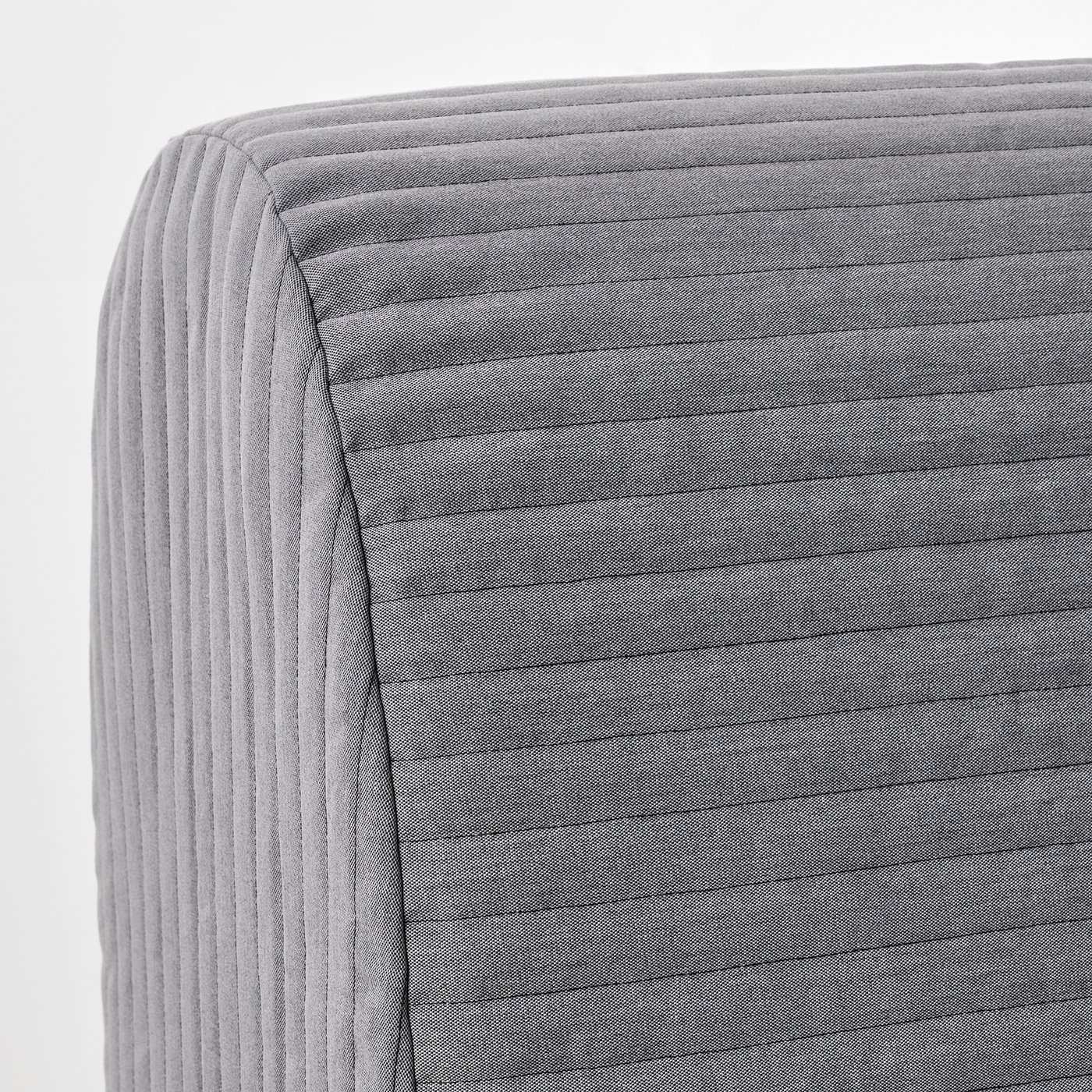 Close-up of a grey fabric sofa-bed with vertical lines, showcasing its plush, quilted texture and sturdy construction.