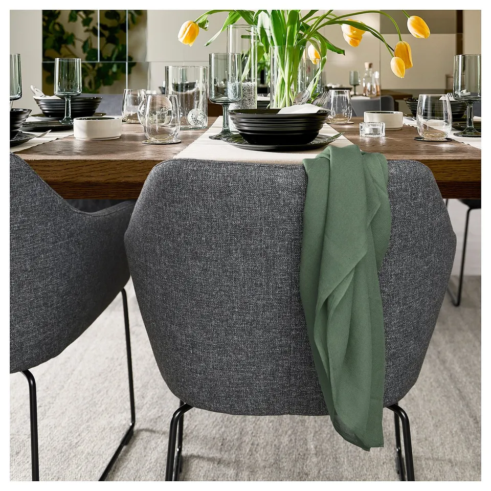 Modern dining setup with grey TOSSBERG chairs, wooden table, black dishes, clear glasses, and yellow tulips.