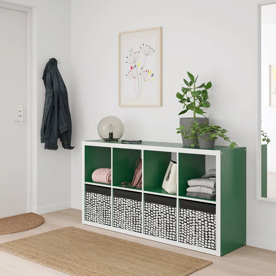 Green DRÖNA box on rug with plant, art, coat.