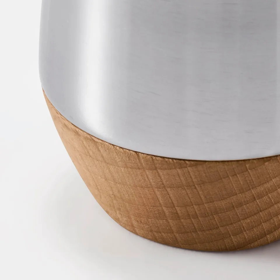Close-up of sleek metal shaker, smooth top, textured wooden base.