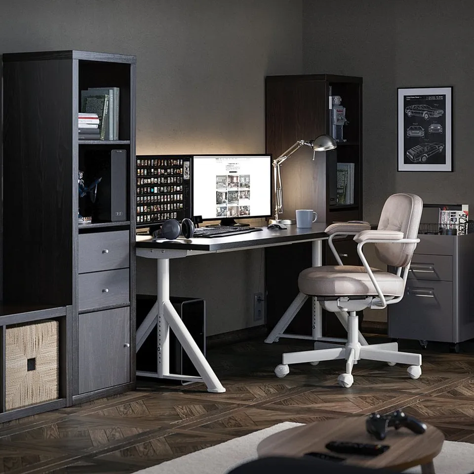 Modern home office with IDÅSEN desk, off-white chair, shelves, and computer. Wood floor, dark walls, and books.
