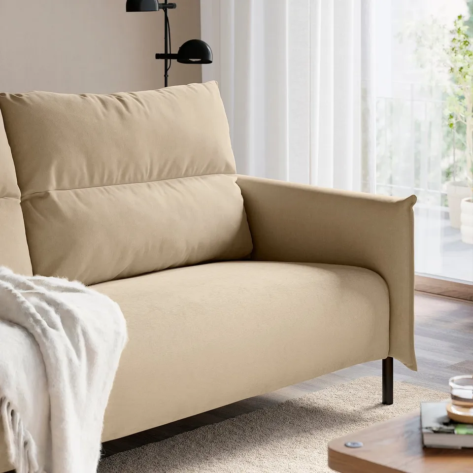 Modern beige sofa with high back, cushions, black legs, near window. Or even shorter: beige sofa with black legs, cushions, by window.