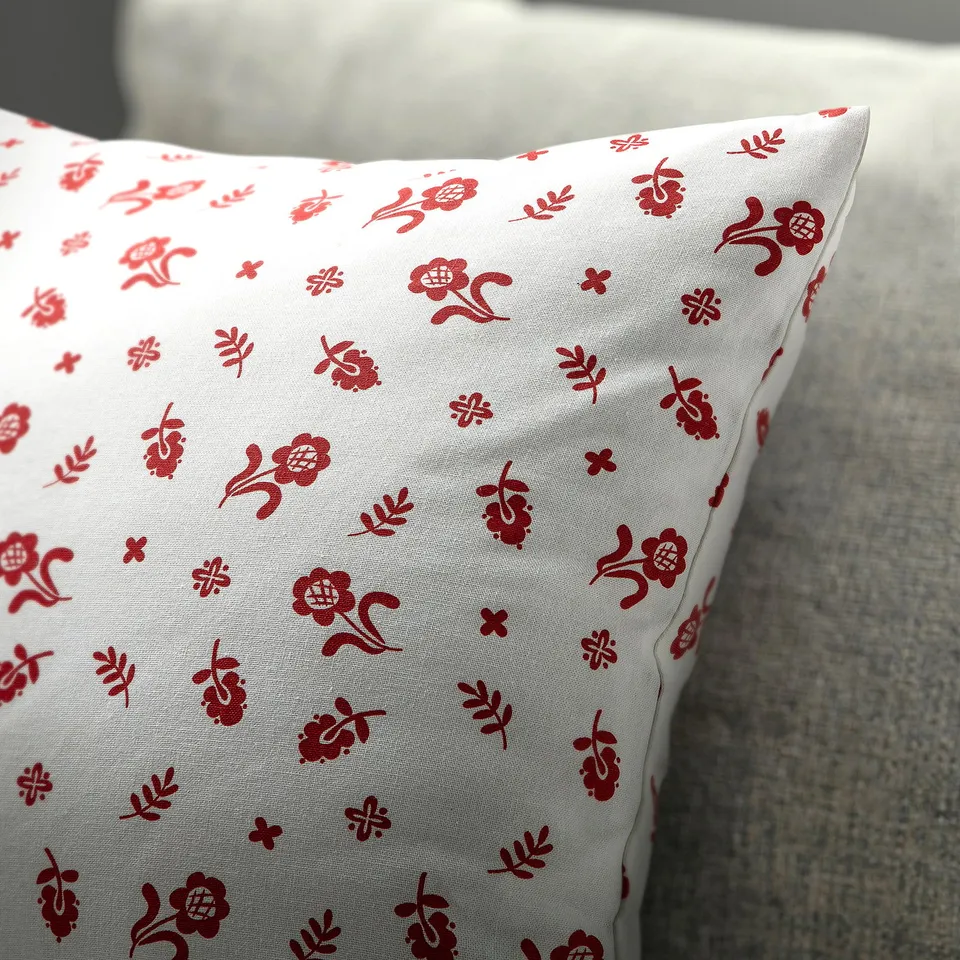 Red floral-patterned cushion on a grey surface. Hidden zip, high-quality cotton.