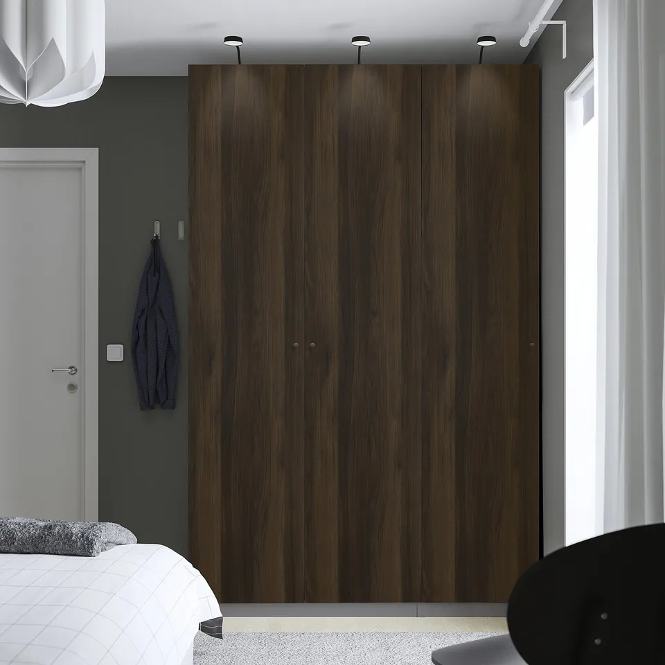 Modern bedroom with large dark PAX wardrobe. White bed, blue jacket by door.