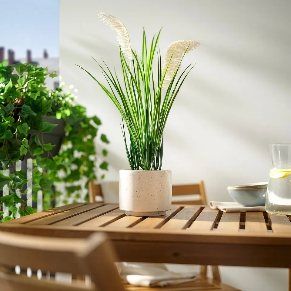 FEJKA plant in grey pot on wooden table outdoors.