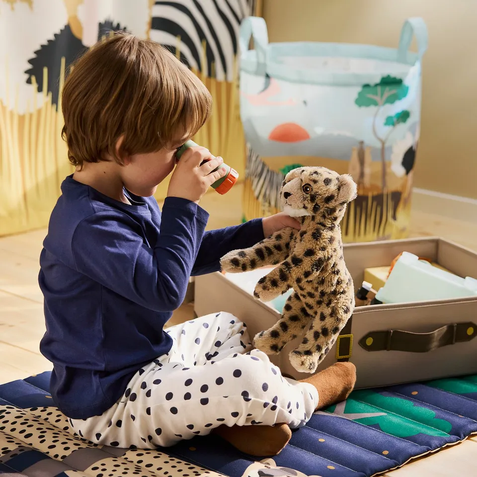 Child plays with cheetah toy and binoculars on colourful rug.