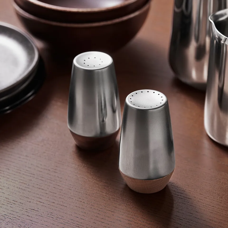 Modern metallic salt & pepper shakers on wooden table, reflecting light.
