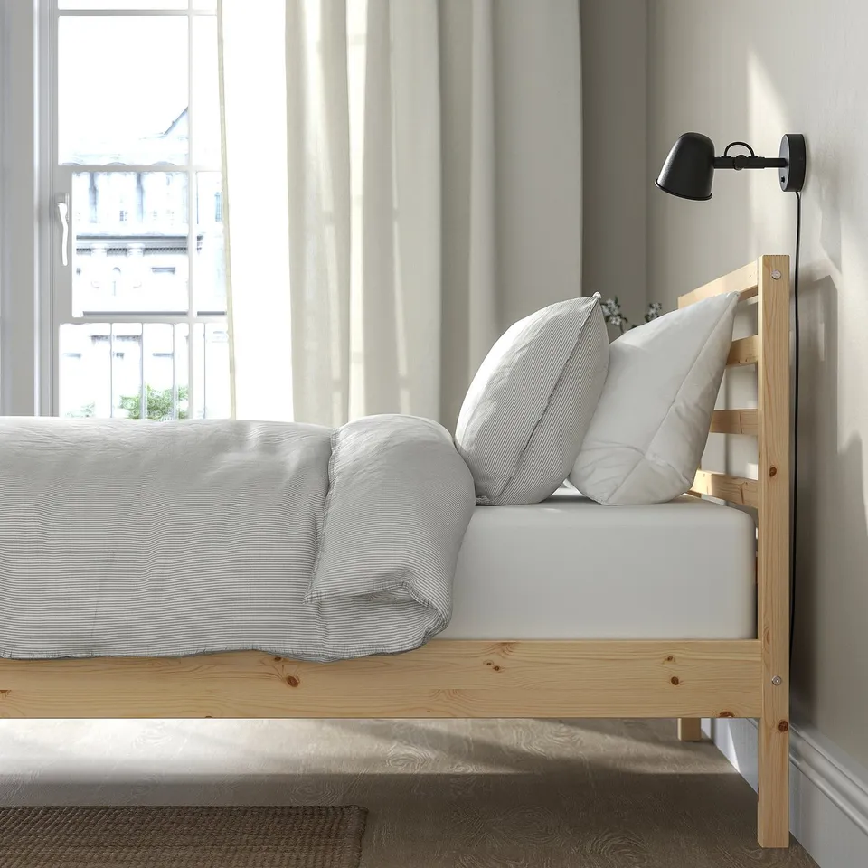 Bedroom scene with a wooden bed frame, white bedding, pillows, and a wall lamp. The bed frame a ladder on its side.