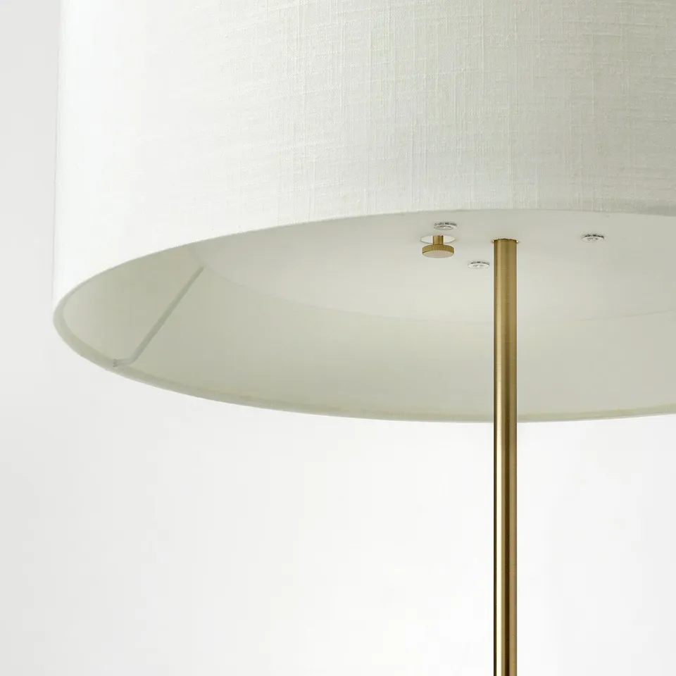 Modern lamp with brass foot, travertine base, and textured shade.
