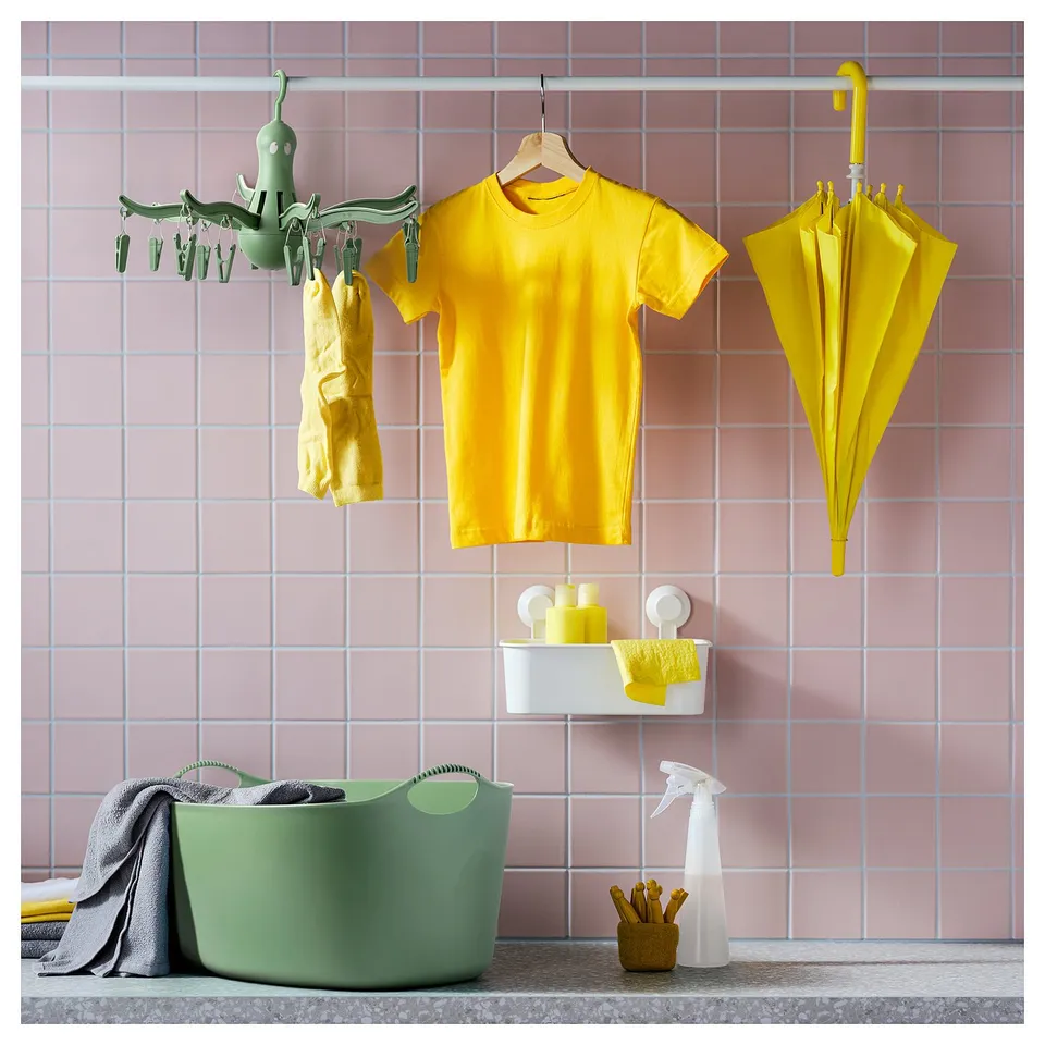Bright laundry room with yellow clothes, green drying rack, dish, umbrella, and green laundry basket on pink tiles.