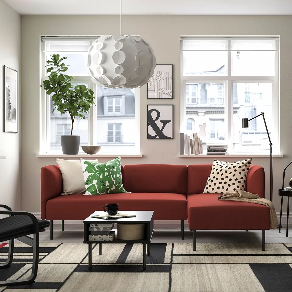 Modern living room with large red LILLEHEM modular sofa, black coffee table, patterned rug, and large windows. Decorative pillows and indoor plant.