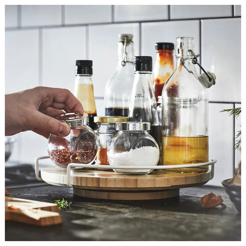 Chefs hand grab spices on lazy susan. Black counter with herbs & cutting boards. White brick kitchen.