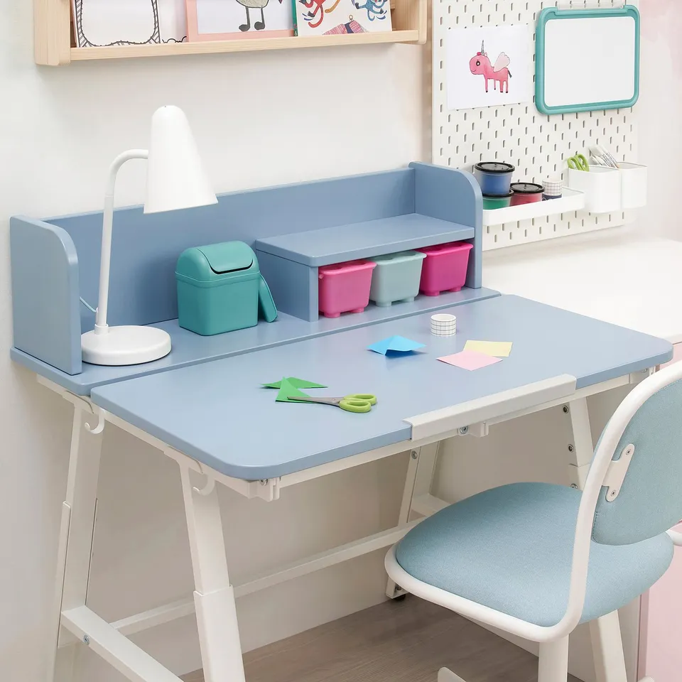 Childs adjustable desk with tiltable top, colourful storage bins, lamp, scissors, and chair.
