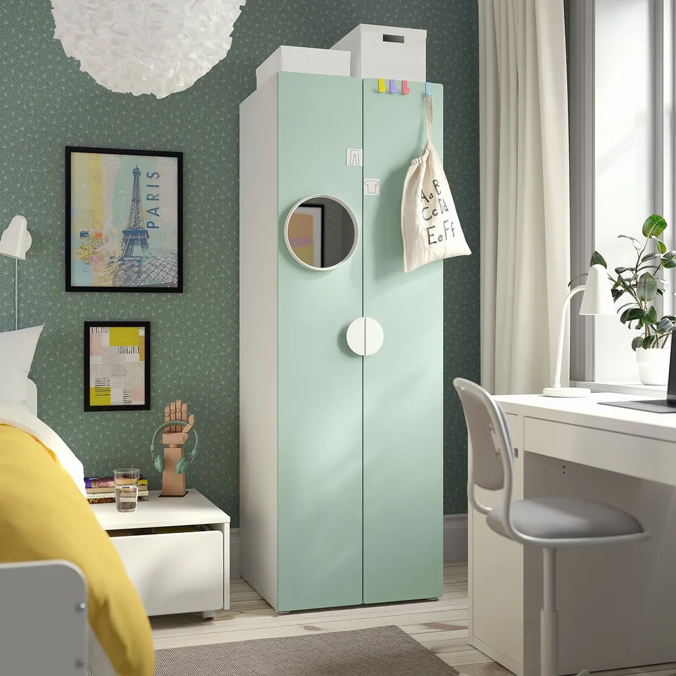 A kids room with a light green SMÅSTAD wardrobe, a desk, and yellow bedding against green patterned walls.
