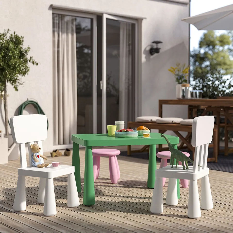 Bright childrens play table set on deck with green table, small white chairs, and stuffed toys. Perfect for outdoor fun.