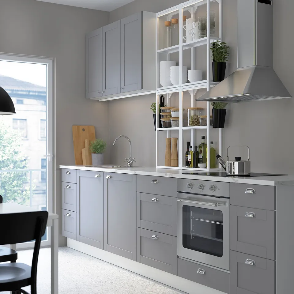 Modern kitchen with white cabinets, stainless steel oven, and grey countertops. Open shelving with white bowls and plants. Open window to city view.