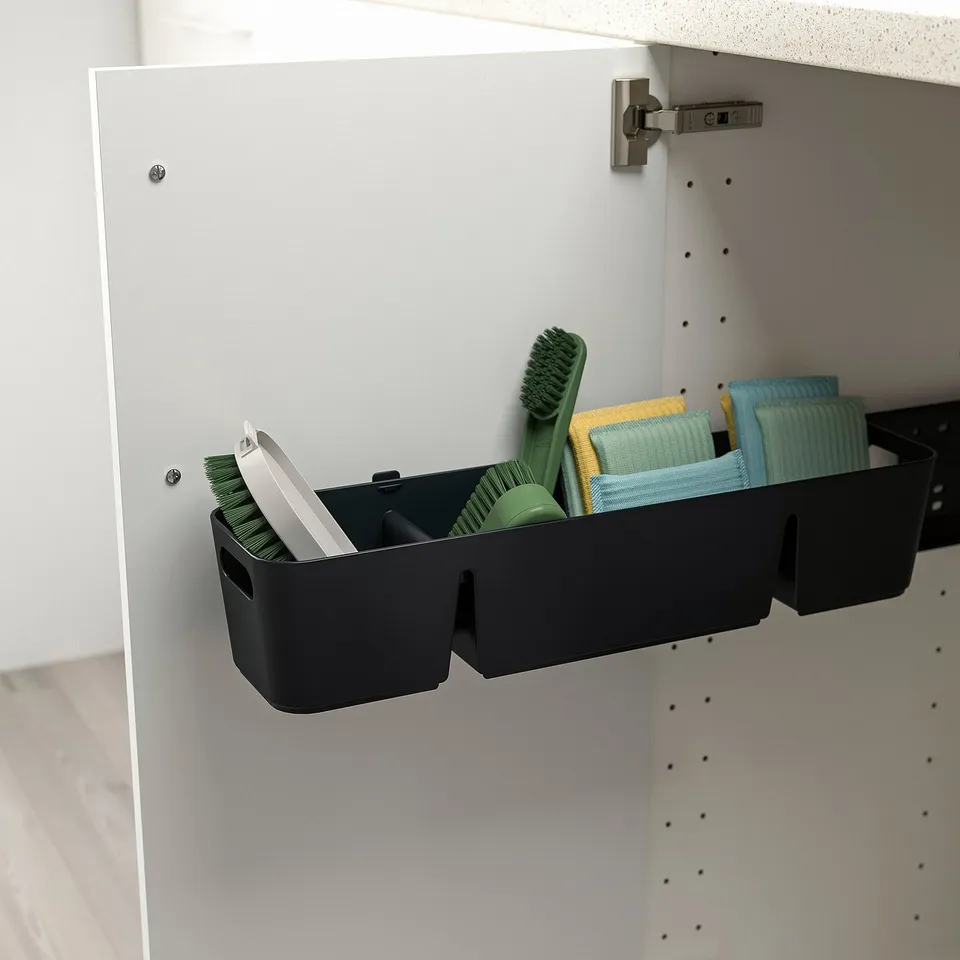 Black storage container inside cabinet, holding cleaning tools like brushes and sponges, designed to pull out for easy access.