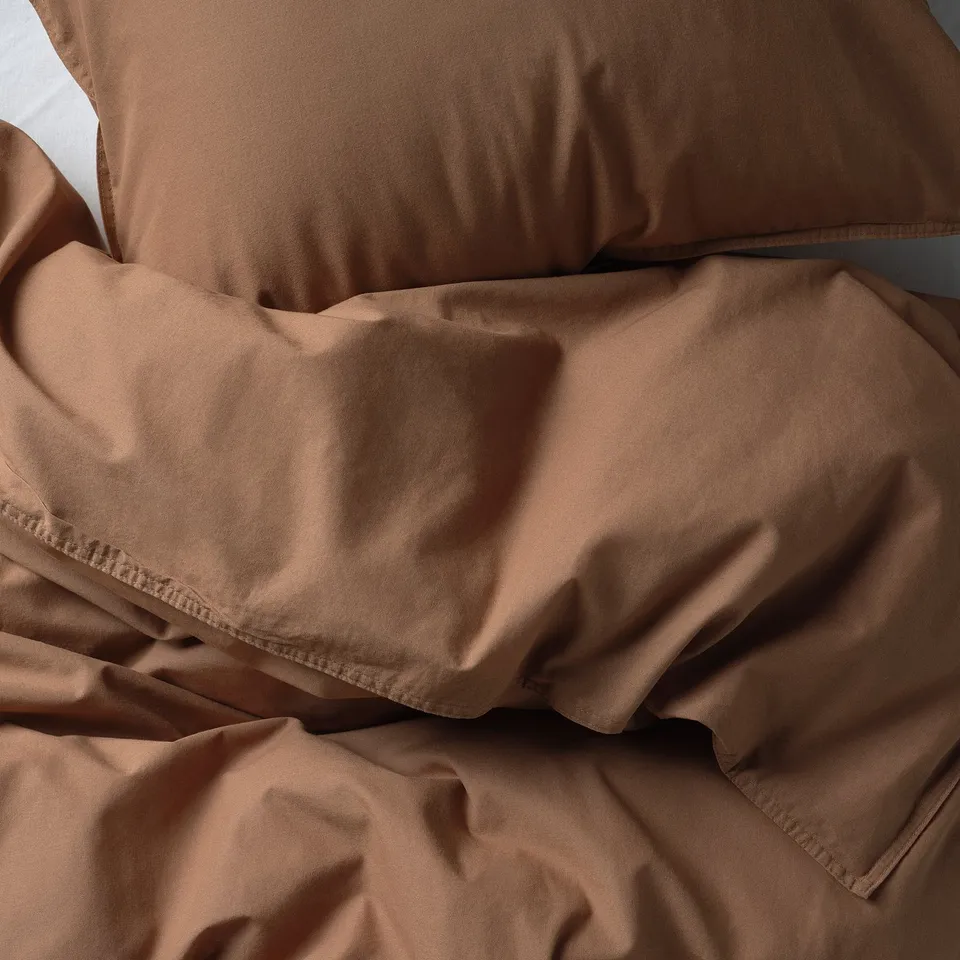 Soft, earth-toned bedding with smooth, wrinkled fabric, likely made of high-quality cotton.