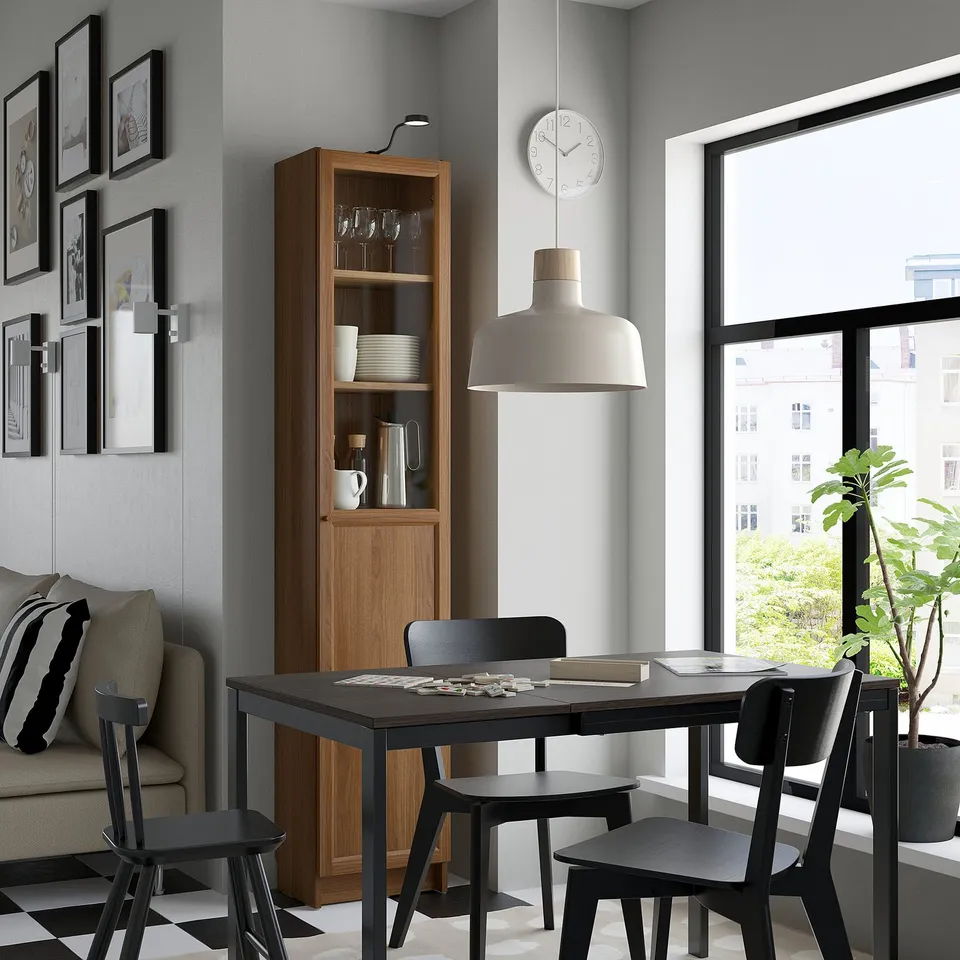 Modern dining area with BILLY bookcase, black chairs, table, white sofa, plant, and clock.